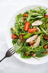 Fresh salad with chicken, tomato and greens (spinach, arugula) on white background top view. Healthy food.