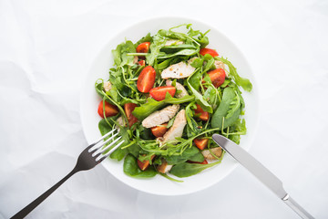 Fresh salad with chicken, tomato and greens (spinach, arugula) on white background top view. Healthy food.