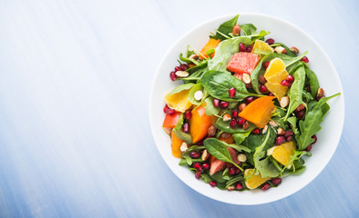 Fresh salad with fruits and greens on blue wooden background top view. Healthy food. Space for text.