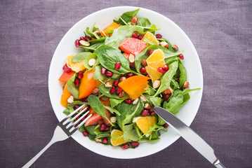 Fresh salad with fruits and greens on dark canvas background top view. Healthy food.