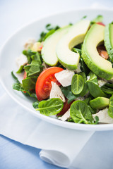 Fresh salad with chicken, tomatoes, spinach and avocado on blue wooden background close up. Healthy food.