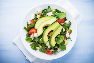 Fresh salad with chicken, tomatoes, spinach and avocado on blue wooden background top view. Healthy food.