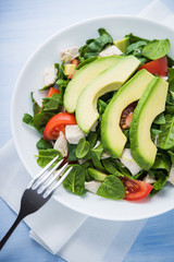 Fresh salad with chicken, tomatoes, spinach and avocado on blue wooden background top view. Healthy food.
