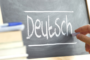 Hand writing on a blackboard in a language class with the word "German" wrote on. Some books and school materials.