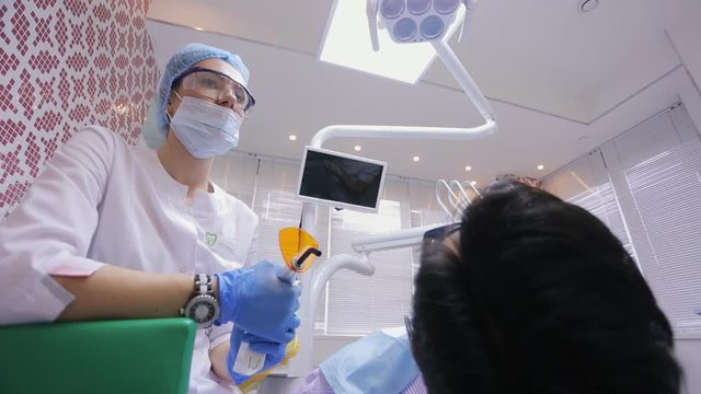Young nurse keeps orange illuminator for photopolymerization process.