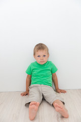 Naklejka premium Little handsome boy with blue eyes, sitting on the floor