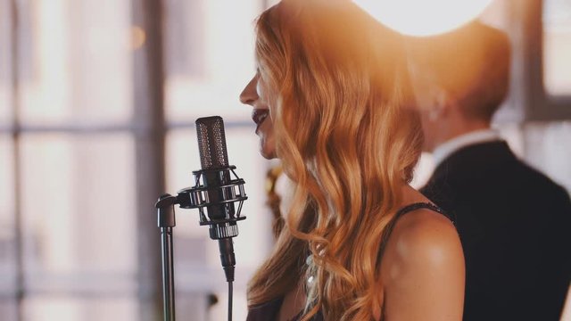 Pretty jazz vocalist with bright make up perform on stage with saxophonist. Retro style. Dance