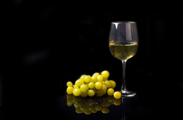 glass of white wine with grapes on a black background with reflection and water drops