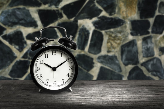 Alarm clock on wood with blurry stone wall in background