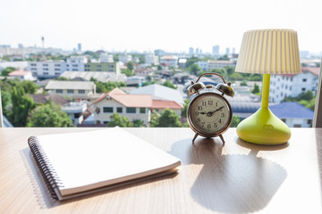 Diary, Clock and desk lamp on table in office on city background.
