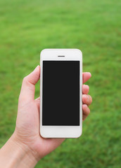 Human hand holding mobile phone against blurred green field background, Vertica