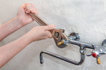 Plumber hands fixing water tap with spanner, close up.