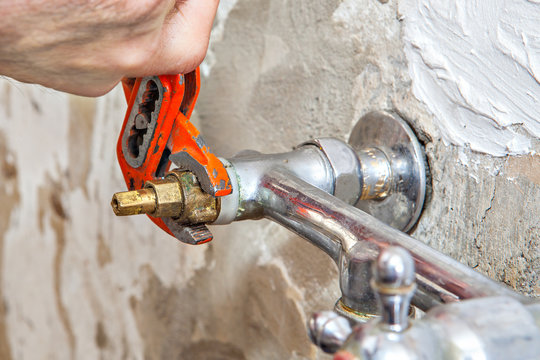 Plumber fixing water tap valve in kitchen, users pliers wrench.