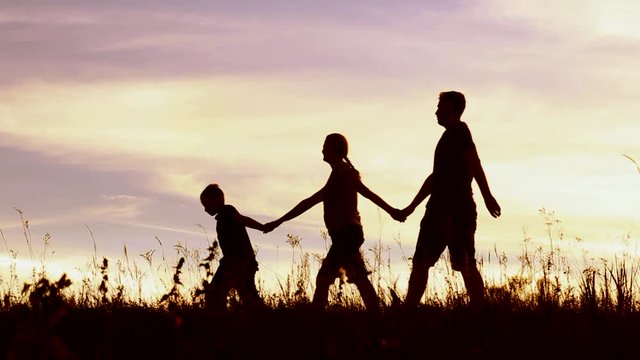 Happy family of mother, father and little child walking outside holding hands over sunset sky background. Portrait of anonymous sunset people having fun in summer landscape. Real time video footage.