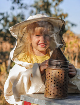 Little girl beekeeper blows smoker for bees