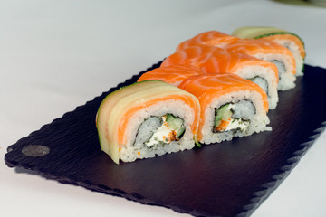 Raw salmon and cucumber sushi roll on dark slate
