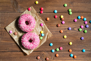 Two pink donuts and colored smarties on wooden table, top view