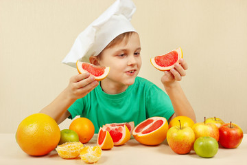 Fototapeta na wymiar Little chef with two slices of grapefruit at the table with fruits