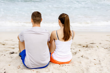 Fototapeta premium Young couple looking at each other while sitting on beach