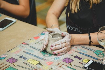 Closeup of hands young woman ceramist working and finishing sculpture with clay on table in workshop