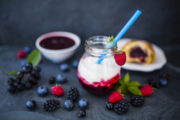 Yogurt with fresh berries fruit and croissant on stone background.