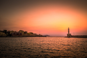 Fototapeta premium The old lighthouse of Chania at sunset, Crete Island, Greece. View of the old venetian port of Chania on Crete island Greece. Tourists relaxing on promenade.