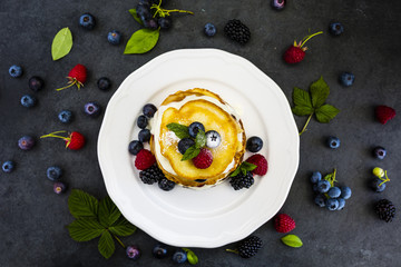 Delicious homemade pancakes with fresh ripe berries served on white plate on stone background.
