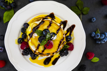 Delicious homemade pancakes with fresh ripe berries served on white plate on stone background.
