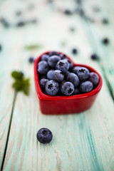 Fresh blueberries in a bowl in the shape of a heart on a wooden background