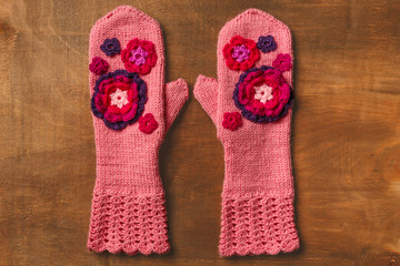 Pink knitted mittens with flowers on wooden background
