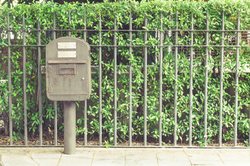 Vintage rusty steel postbox in front of metal fence and green he
