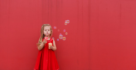 little girl in red dress blowing soap bubbles on the  background