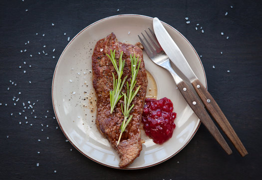 Grilled steak with rosemary and  cranberry sauce on a dark background.
