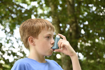 Boy with Asthma inhaler. Young boy using a blue asthma inhaler - obrazy, fototapety, plakaty