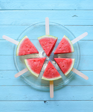 Cheerful summer image of watermelon wedges on sticks on a blue b