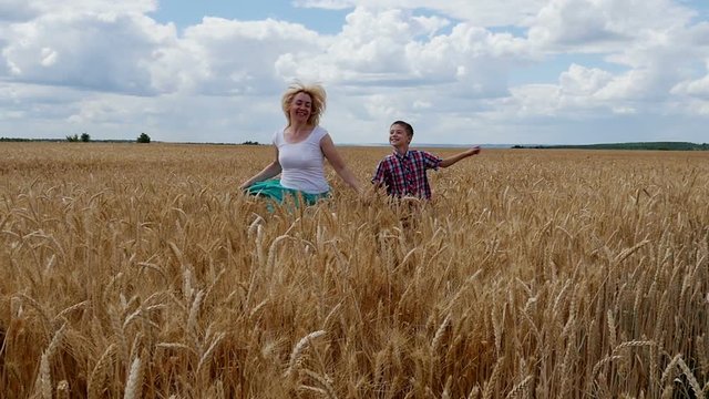 Mother and son running on the wheat field. Happy family in summer field