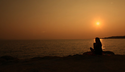 Naklejka na ściany i meble Girl is waiting on seaside during beautiful sunset