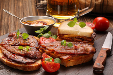 Sandwich with fried bacon and beer on wooden background