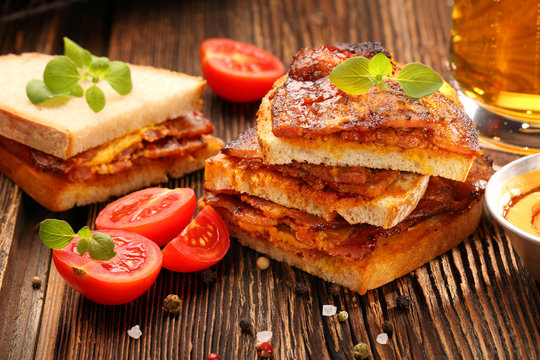 Sandwich with fried bacon and beer on wooden background