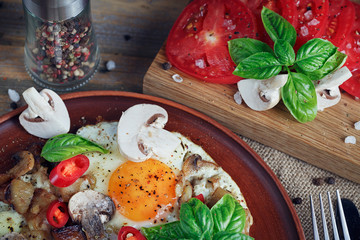 Fried eggs with mushrooms, tomatoes and basil on rustic wooden t