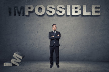 Obraz premium Front view of a buisnessman standing with folded arms under big 3d concrete word 'possible'
