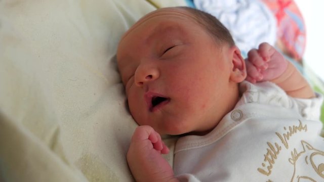 Lovely infant sleeping in a crib, moving the head and trying to open his eyes