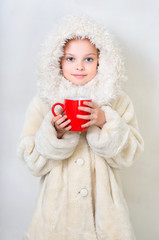 Smiling little girl in winter clothes with a red cup of hot drin