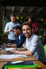 Portrait of happy businessman smiling for camera. Handsome man working on laptop computer in restaurant, cafe or modern office interior.