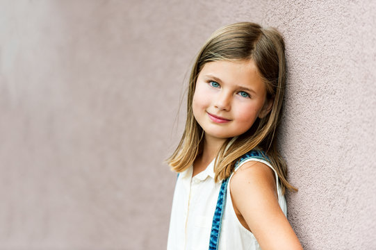 Close up portrait of a cute little girl of 7-8 years old leaning to pink wall