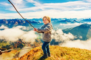 Portrait of a cute little boy in mountains, wearing grey jacket and mountain boots,...