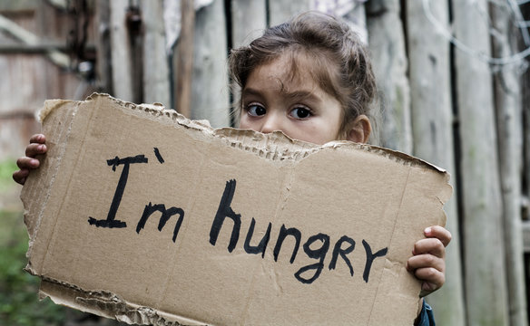 Little girl holding a sheet of cardboard. On the cardboard label "I am hungry." The child is three years.
