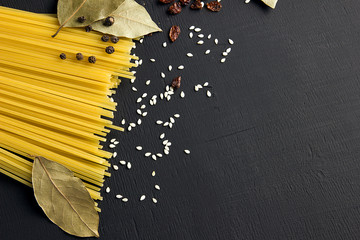 Raw spaghetti and Bay leaf, barberry, pepper, sesame seeds on black wooden background, top view place for text