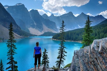 Woman on cliff at scenic lake and mountains. Moraine Lake in Rocky Mountains. Banff National Park, Alberta, Canada. 