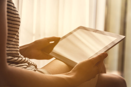 Close up on woman hands holding blank tablet and reading in cozy home space.